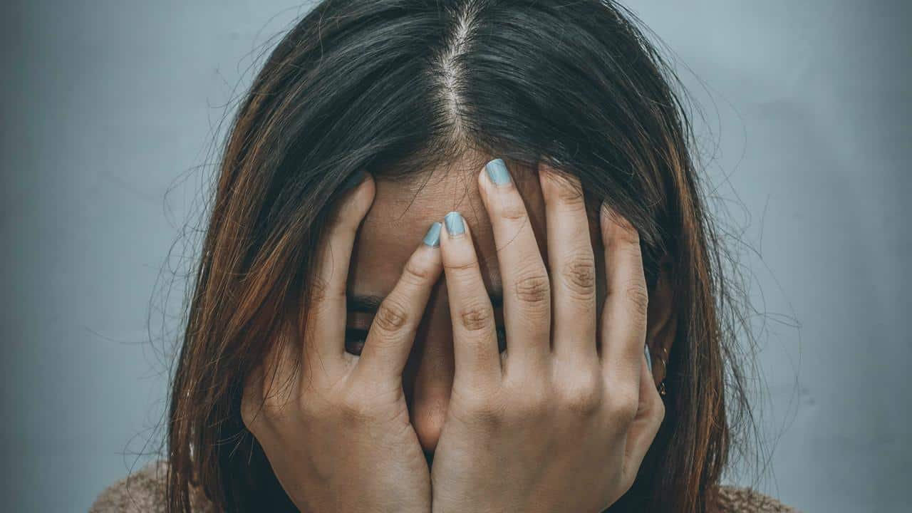 A person covering their face with their hands, appearing upset.