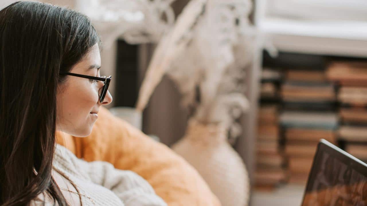 A woman wearing glasses using a laptop indoors.