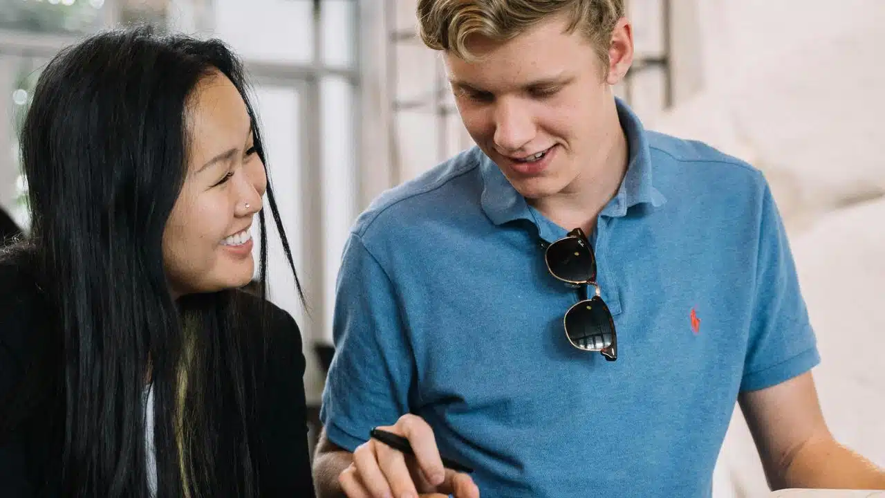 A pair of people smiling and looking at something together indoors.