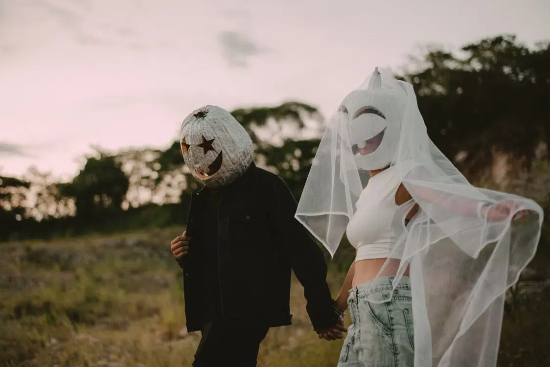 Couple in pumpkin heads holding hands as they walk.