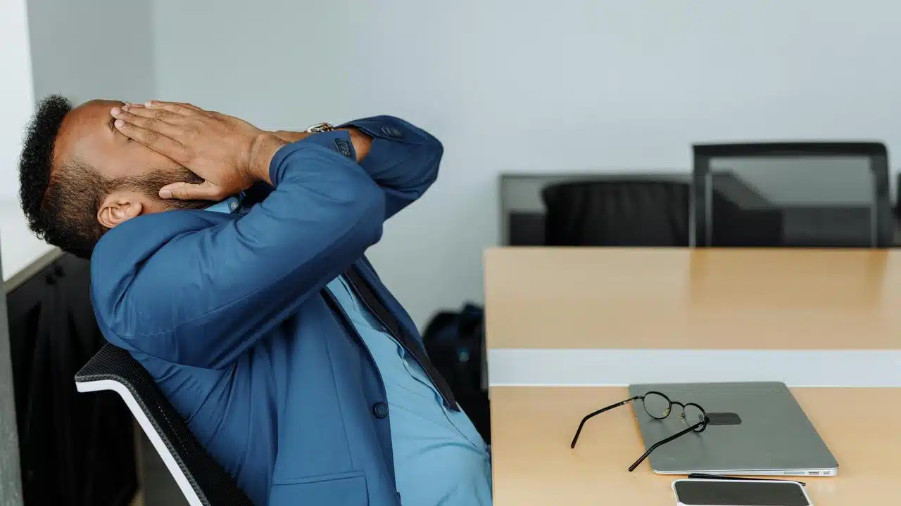 A man leaning back in a chair with his hands on his face, looking stressed.