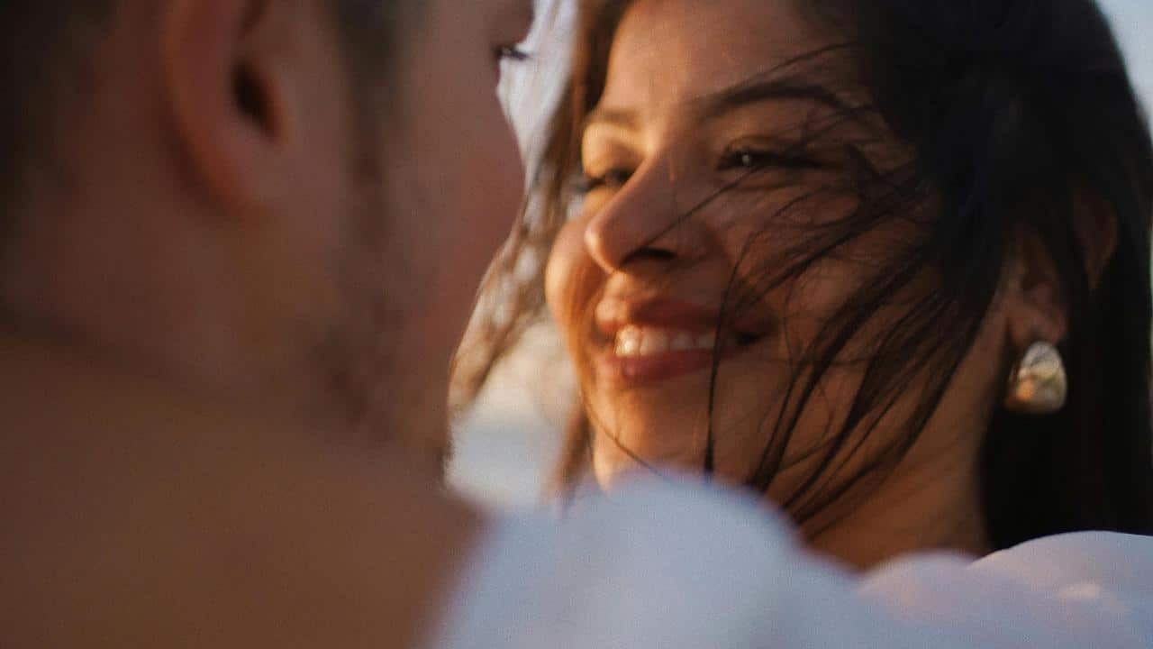 A woman smiling warmly at someone with wind blowing through her hair.
