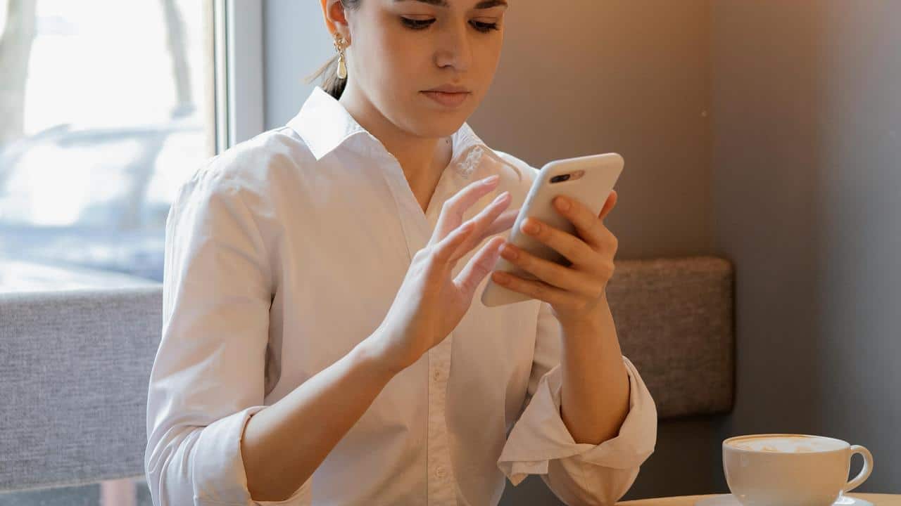 A woman using her smartphone while sitting at a cafe table with a cup of coffee.