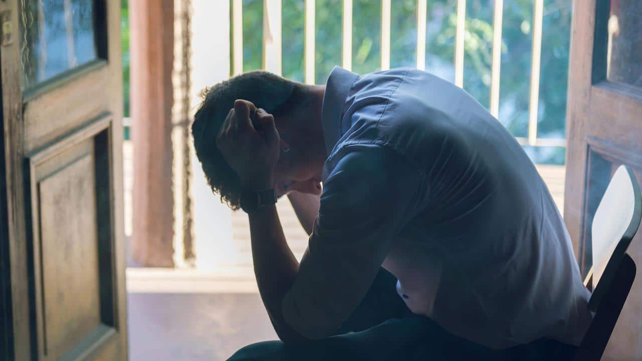 A man sitting with his head down and hand on his forehead near a doorway.