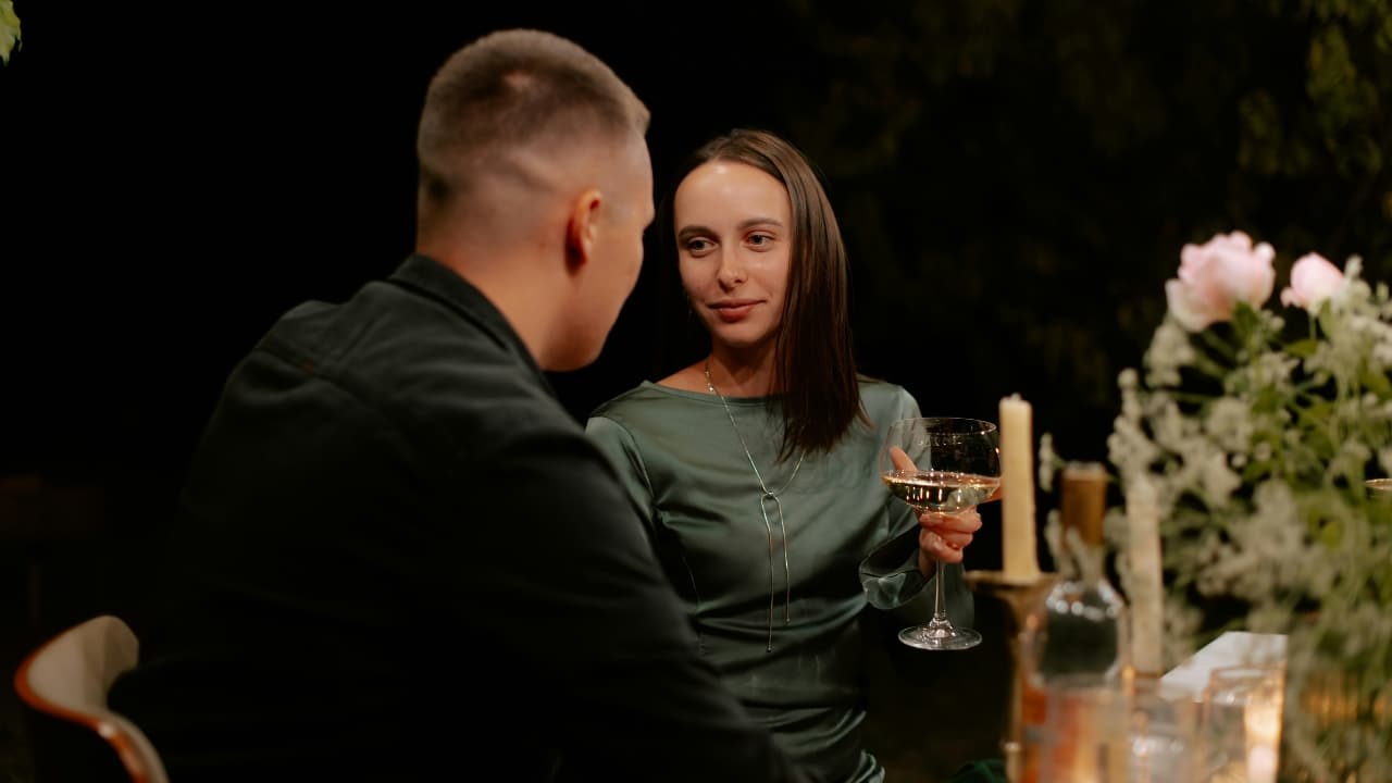 A woman in a green dress holds a wine glass while looking at a man.