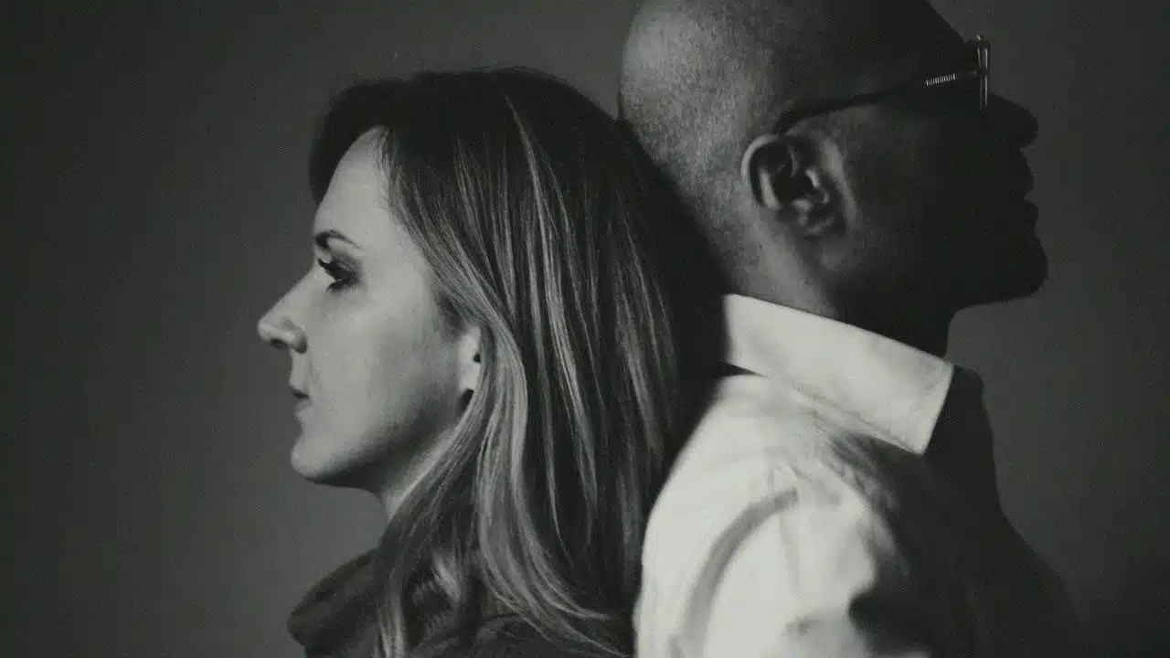 A black and white profile photo of a woman and man leaning back to back.