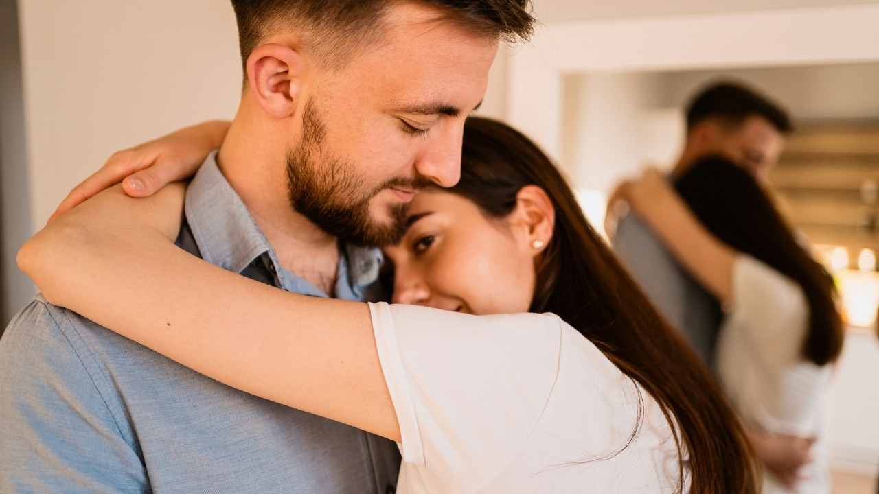 A woman wraps her arms around a man's neck while resting her head on him.
