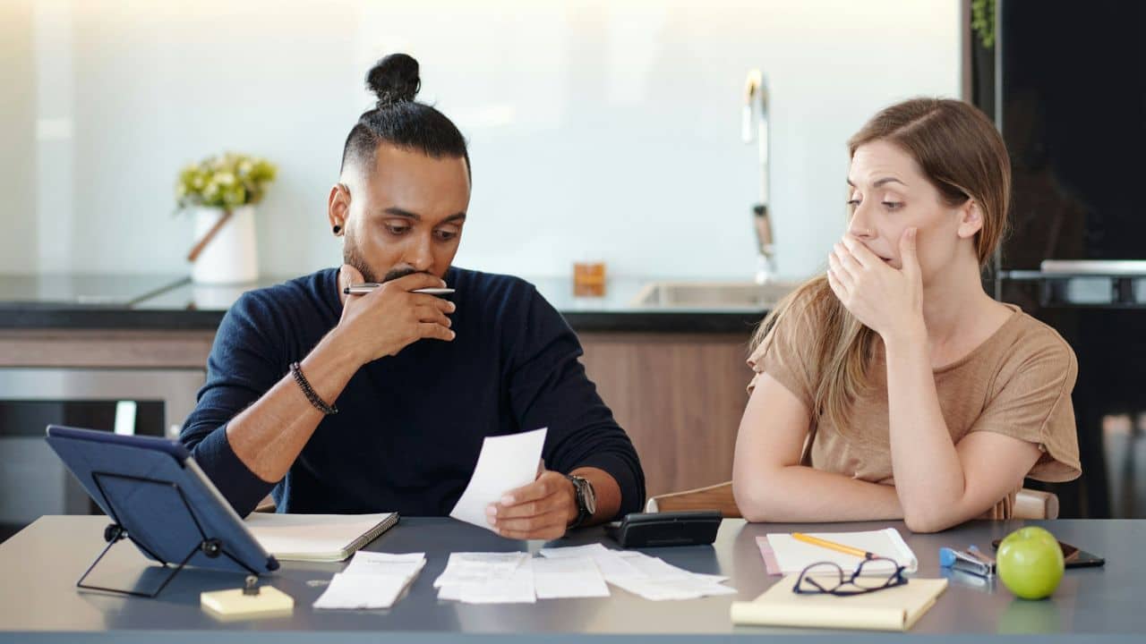 A man and woman sit at a table looking at various receipts and a digital tablet.