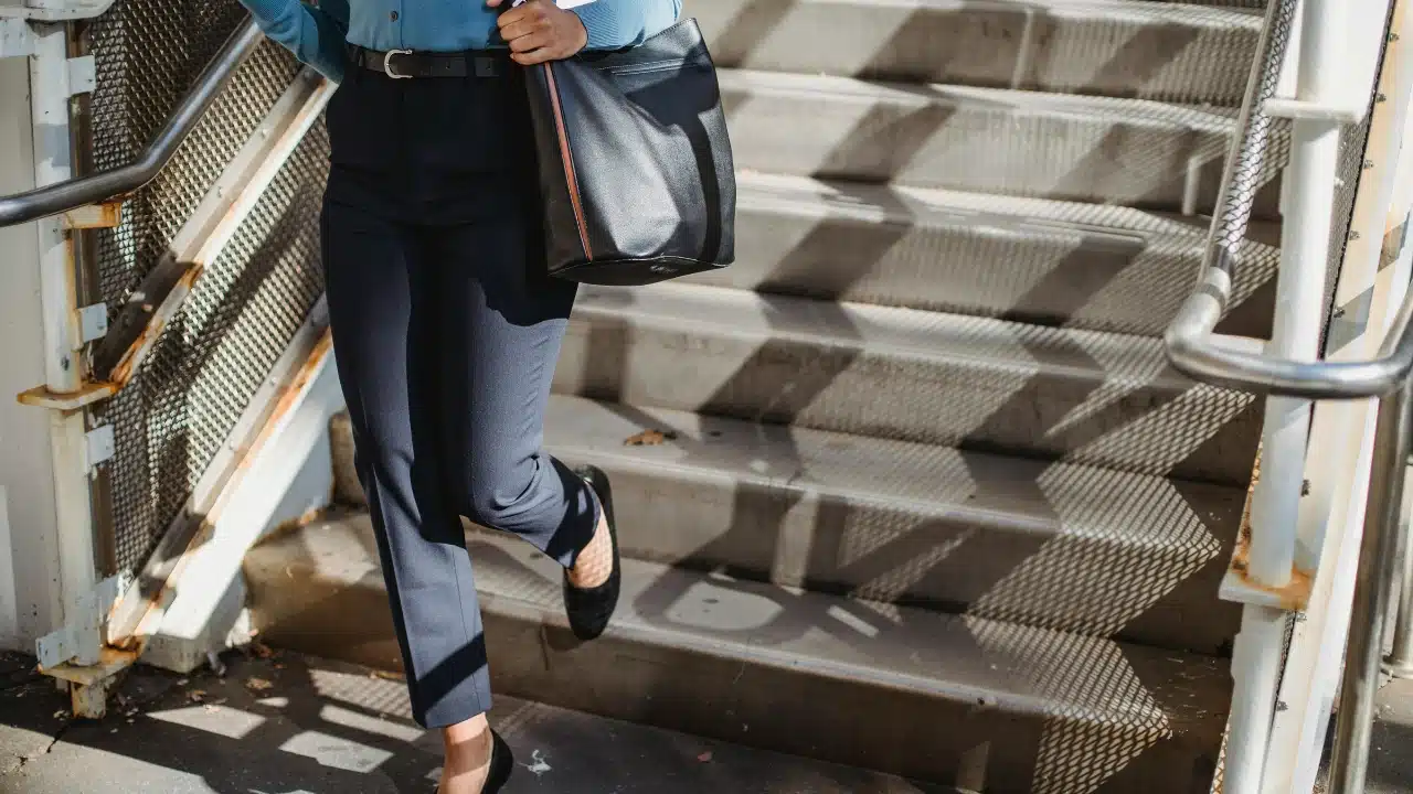 A person wearing dark trousers and carrying a black bag walks down a set of stairs.