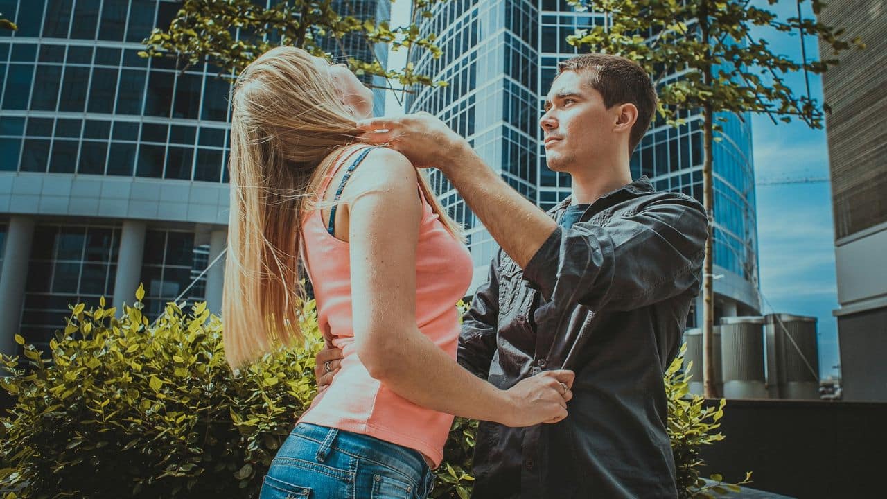 A man holds a woman's neck and waist while she leans her head back outdoors.
