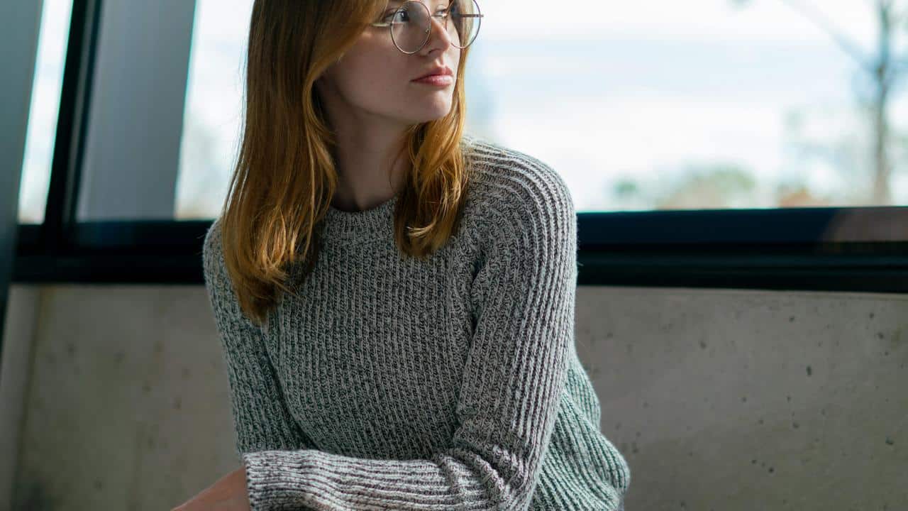 A woman wearing glasses and a gray sweater looks to the side.