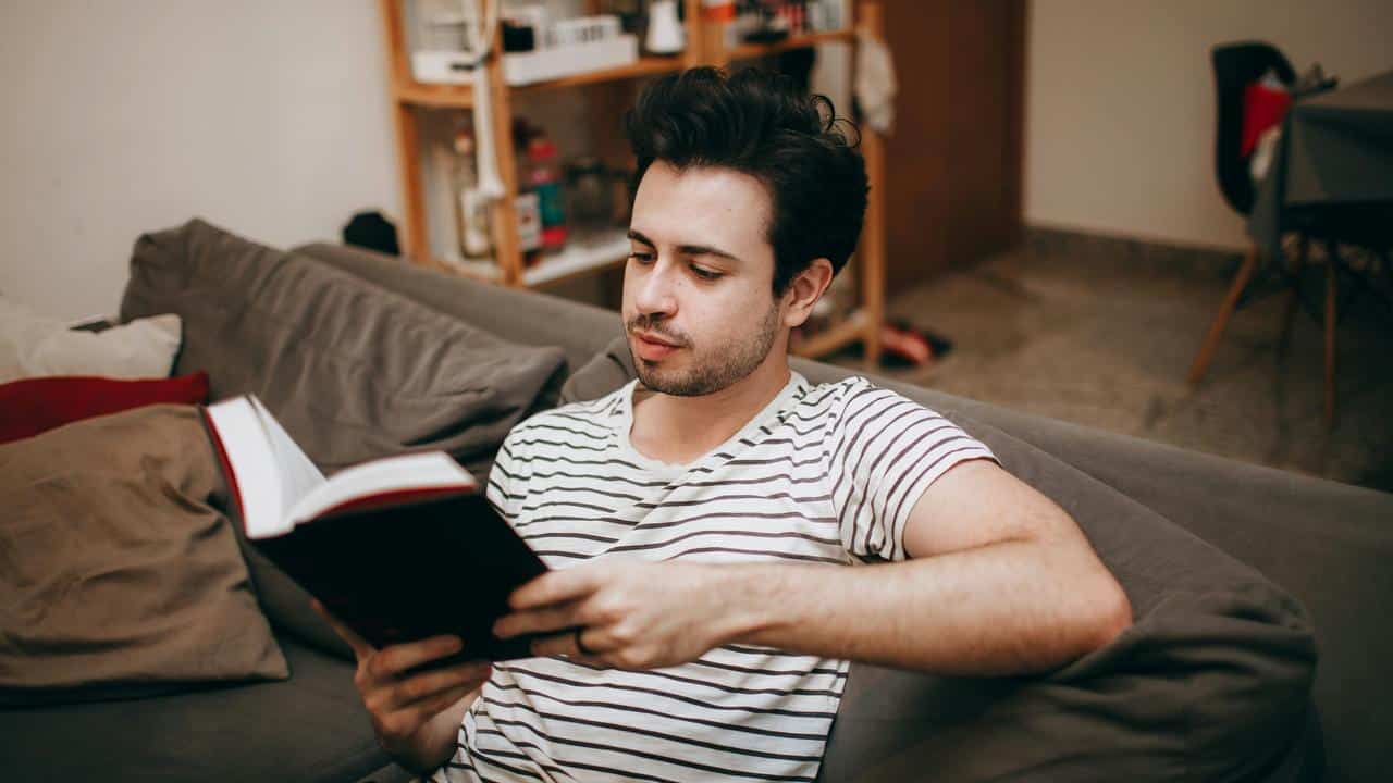 A man sitting on a couch reading a book.