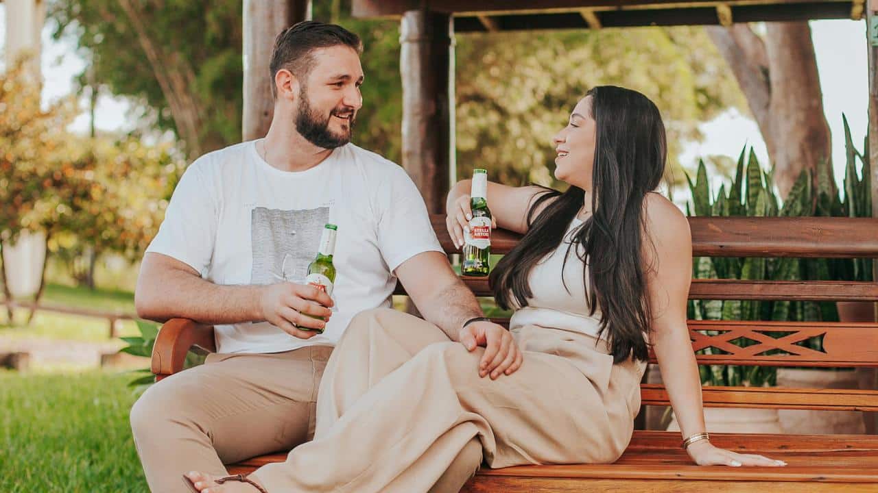 A couple sitting on a bench while sharing drinks outdoors.