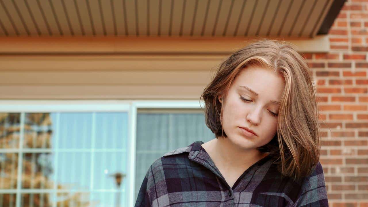 A woman looking down pensively outside a brick house.