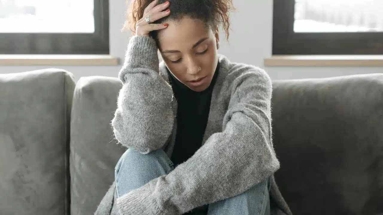 A woman sitting on a couch with her head in her hand, looking distressed.