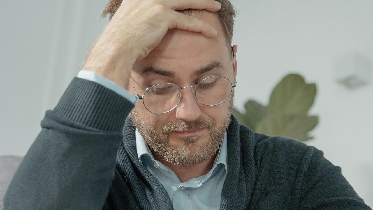 A man wearing glasses holding his head and looking stressed.