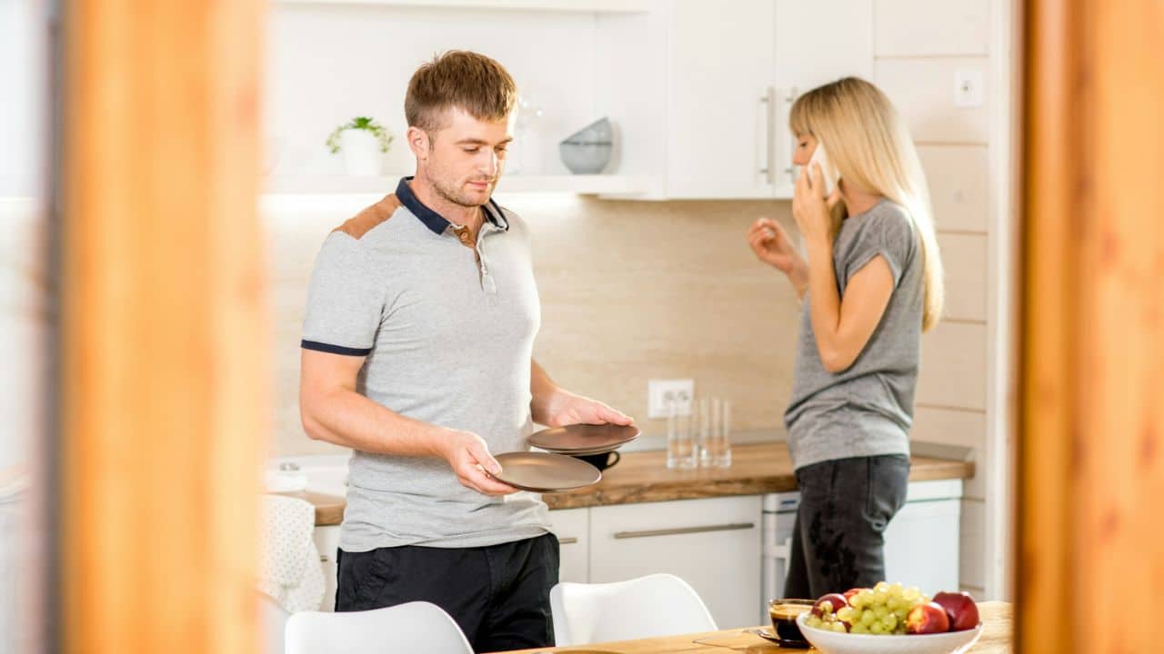 A man holds two plates in a kitchen while a woman talks on a mobile phone.
