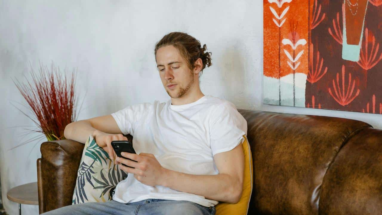 A man sitting on a couch, focused on his phone in a cozy living room.