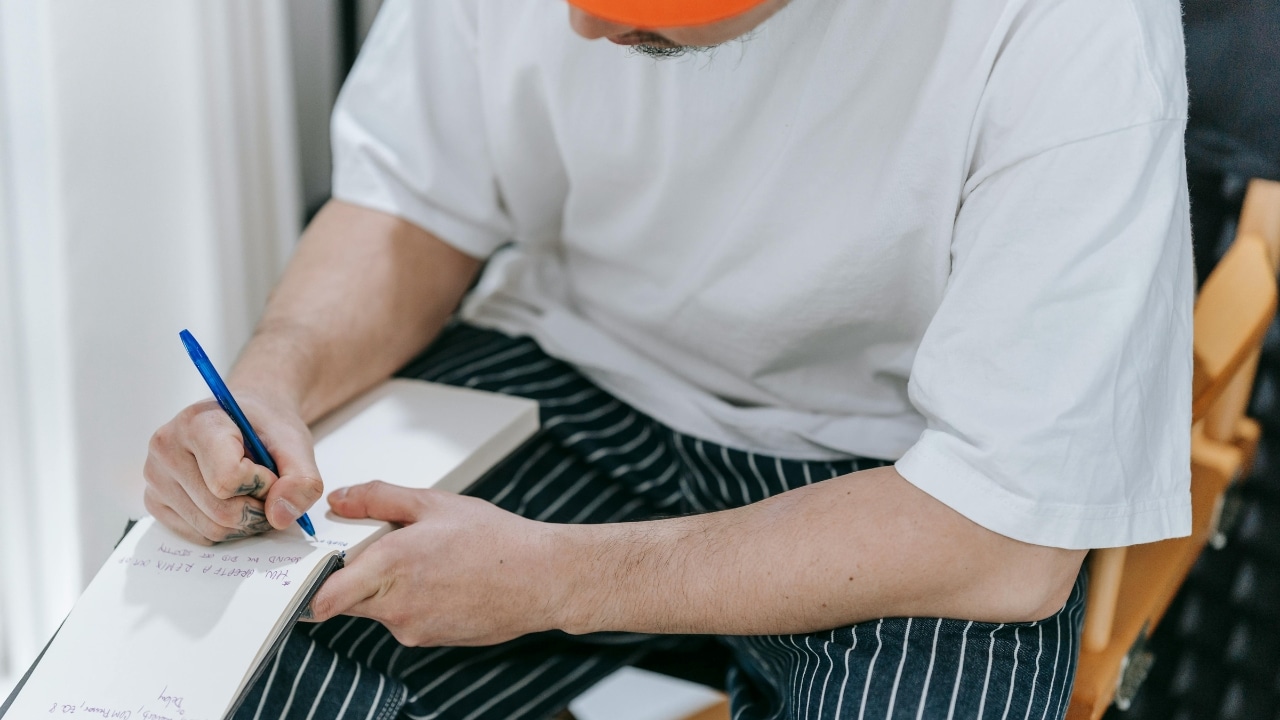 Close up of a person in a white shirt writing in a notebook with a pen.