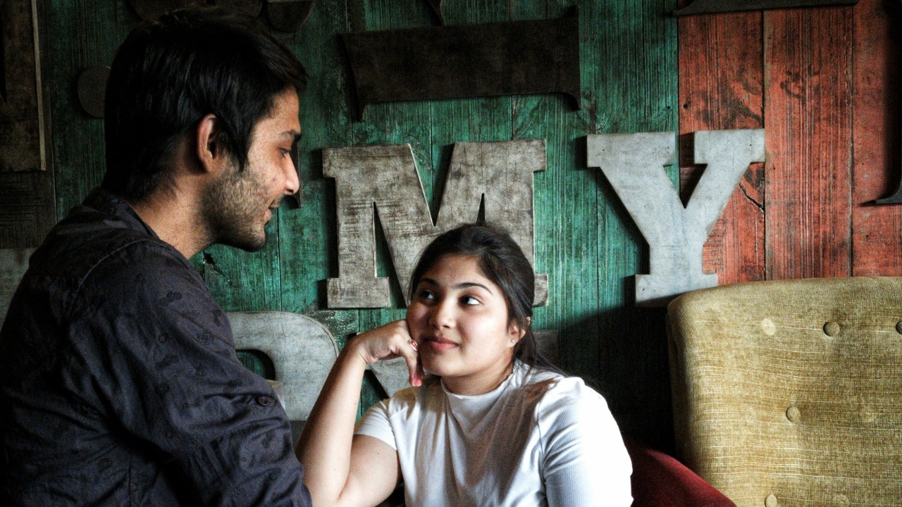 A woman rests her chin on her hand and looks upward while talking to a man.