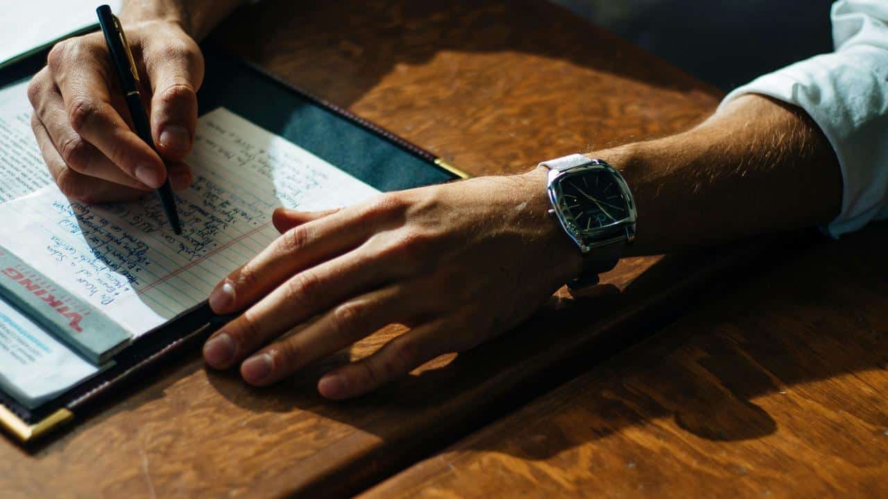 A person writing notes on paper at a wooden desk.