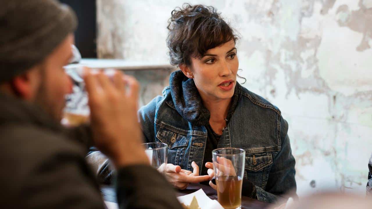 A woman talking animatedly at a table with drinks while others listen.