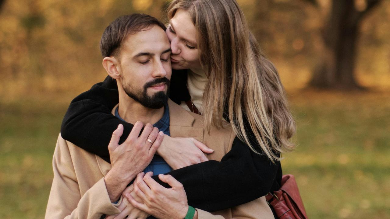 A woman hugging and kissing a man on the cheek outdoors.