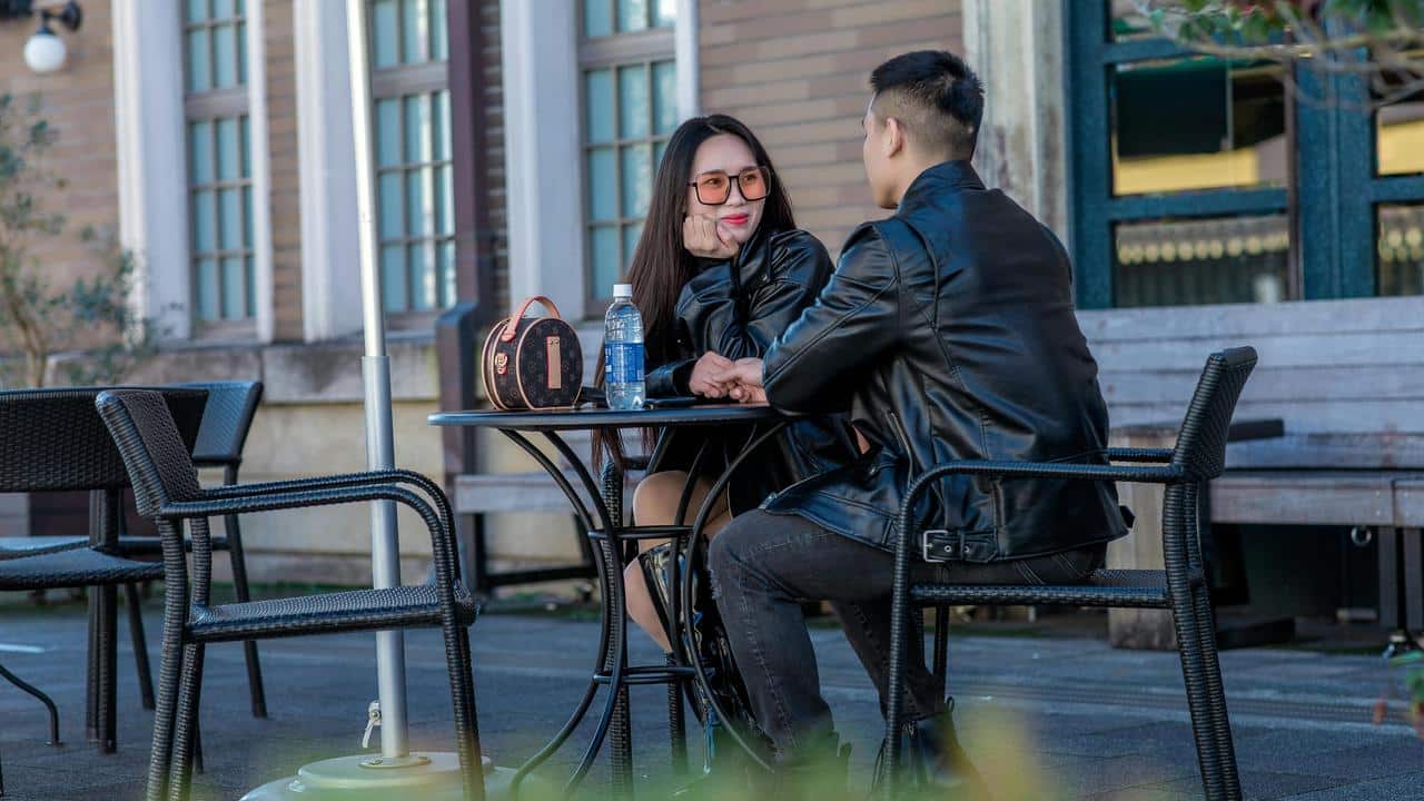 A couple sitting at an outdoor table talking and smiling at each other.