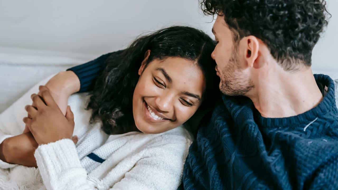 A smiling couple cuddling closely on a couch.