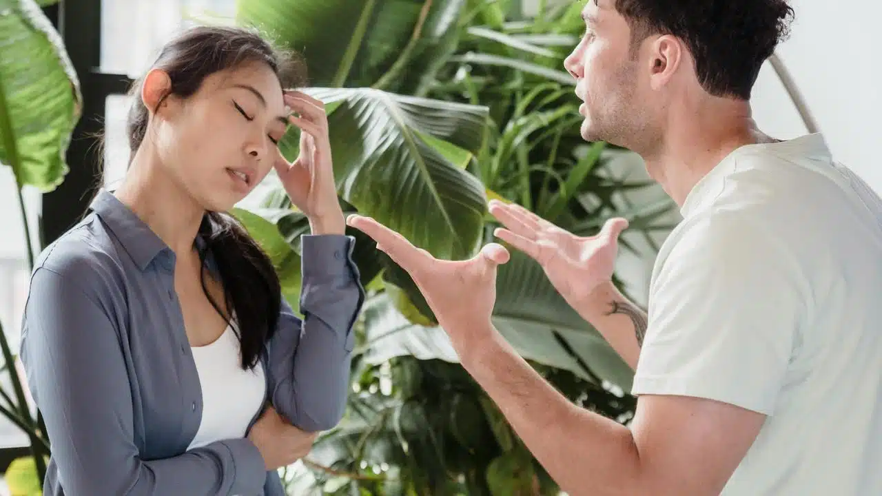 A couple arguing, with the woman holding her head in frustration.