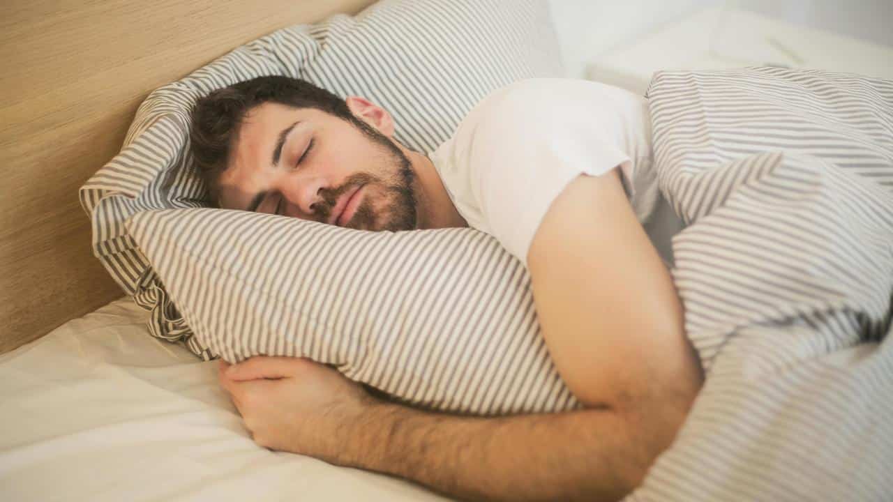A man sleeping in bed while hugging a striped pillow.