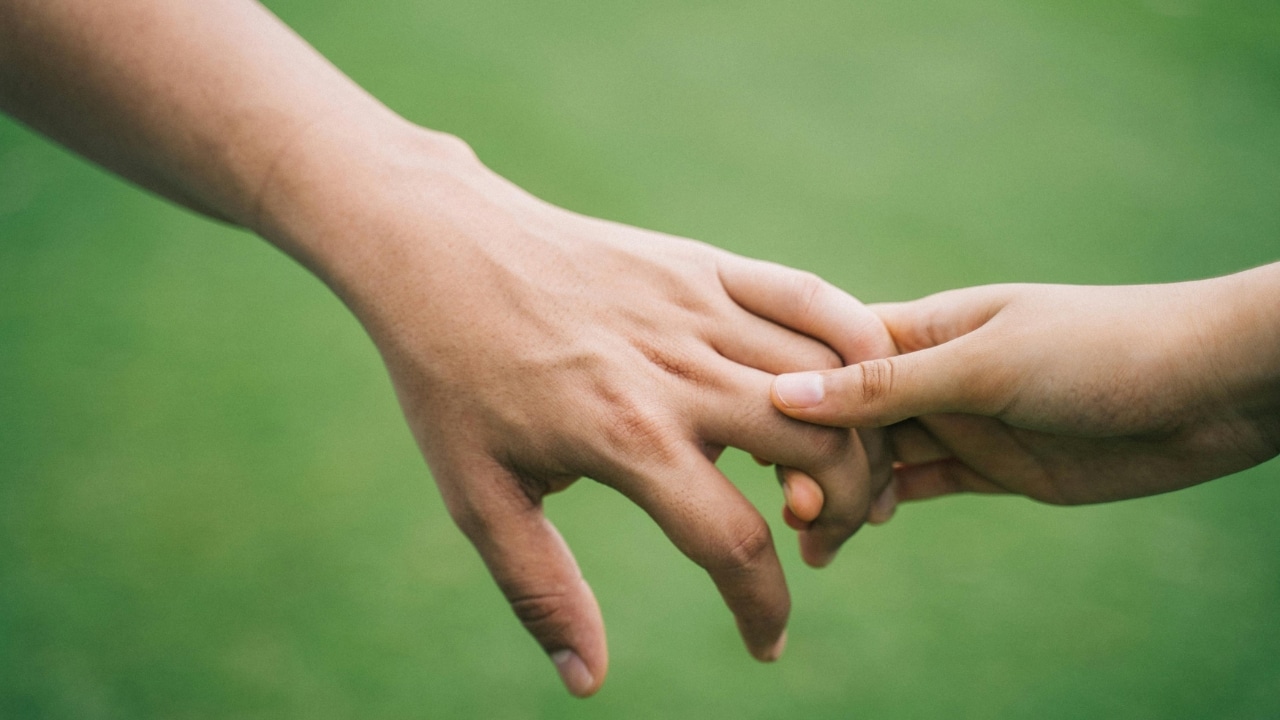 Close-up of two hands briefly touching fingers against a blurred green grass background.