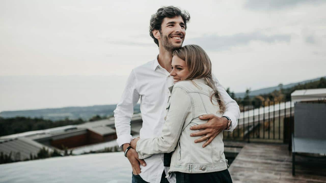 A man hugging his wife in a happy mood while they are standing outdoors.