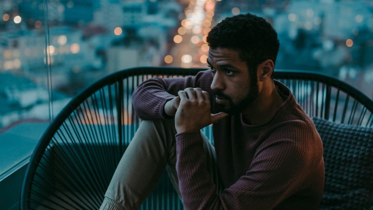 Thoughtful man sitting in a chair, looking out at city lights at night.