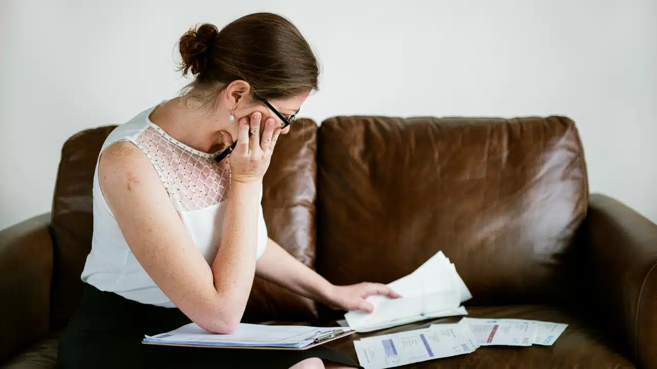 A woman sitting on a leather sofa looks down while reviewing several papers and invoices.