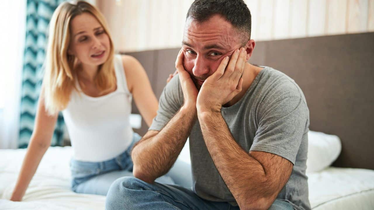 A man holds his face in his hands while a woman speaks to him.