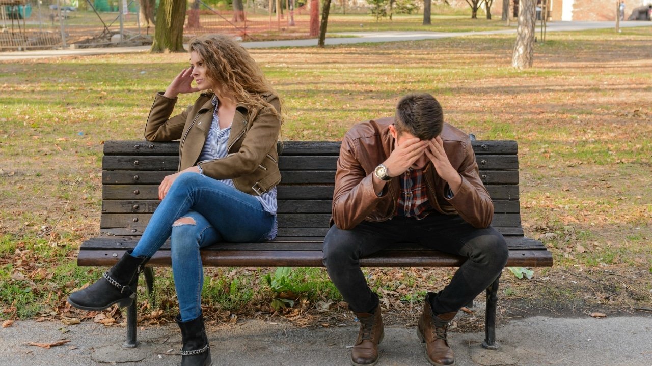 A man sits on a park bench with his head in his hands near a woman.