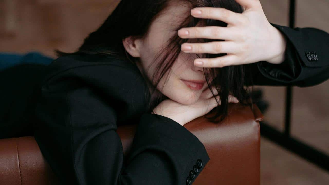 A person with dark hair partially covering their face rests on a chair.