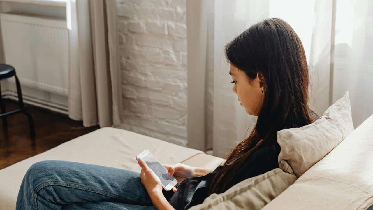 A woman sitting on a couch, looking at her phone in a softly lit room.