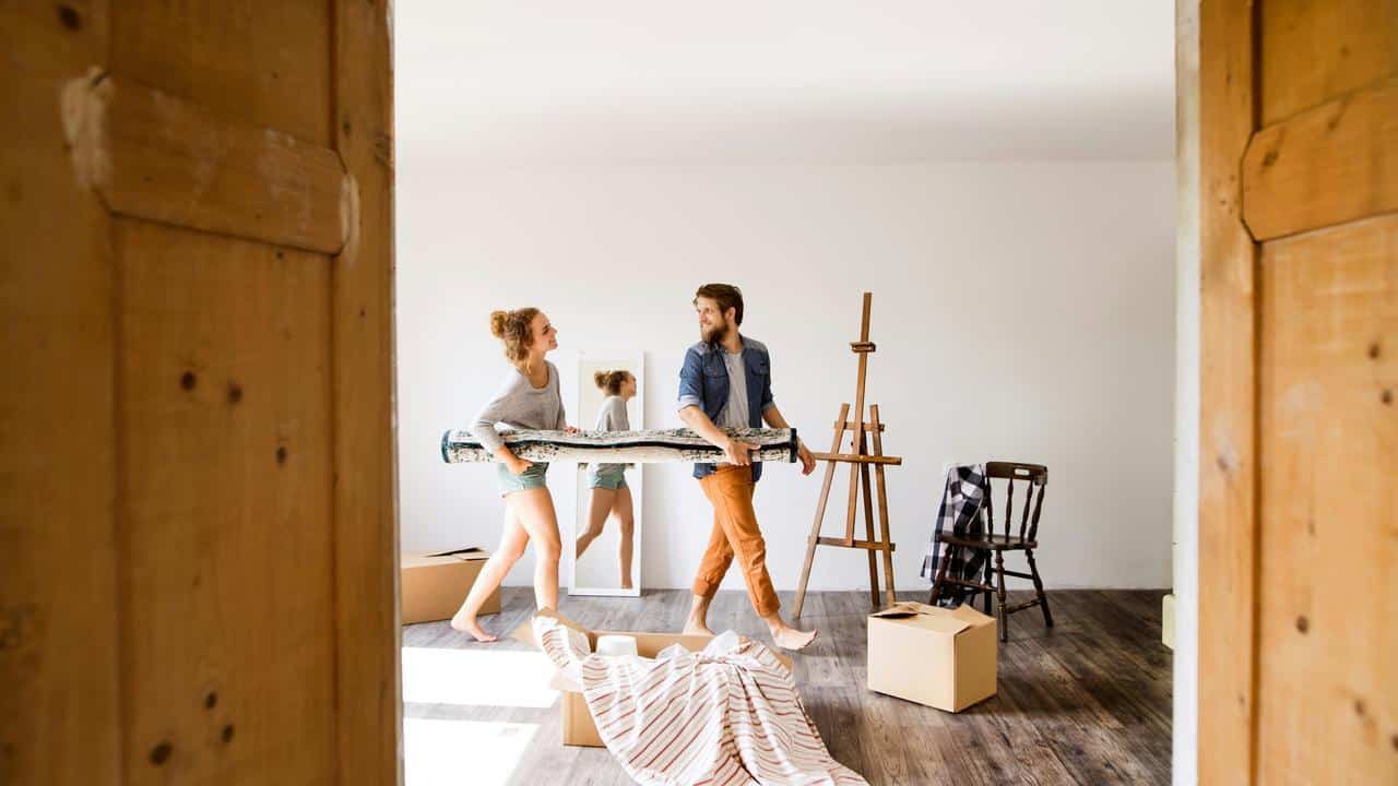A couple carrying a rolled-up rug while setting up a new home.