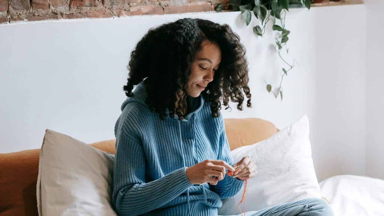 A woman knitting on a couch indoors.