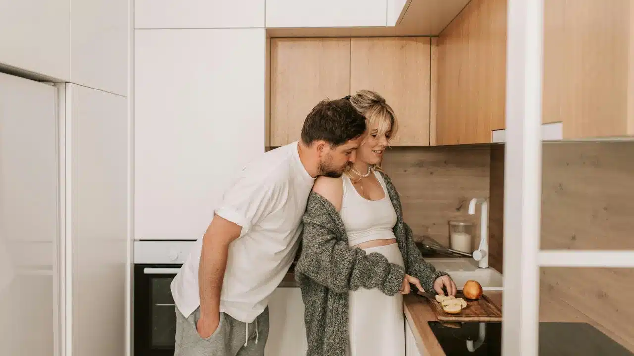 A couple in a kitchen, slicing fruit together.