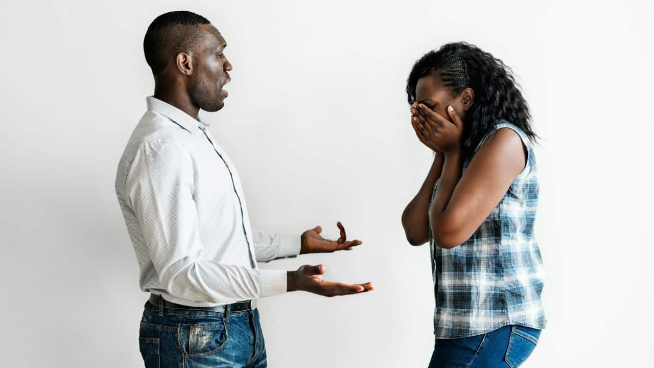 A man with an open mouth gestures toward a woman covering her face with hands.