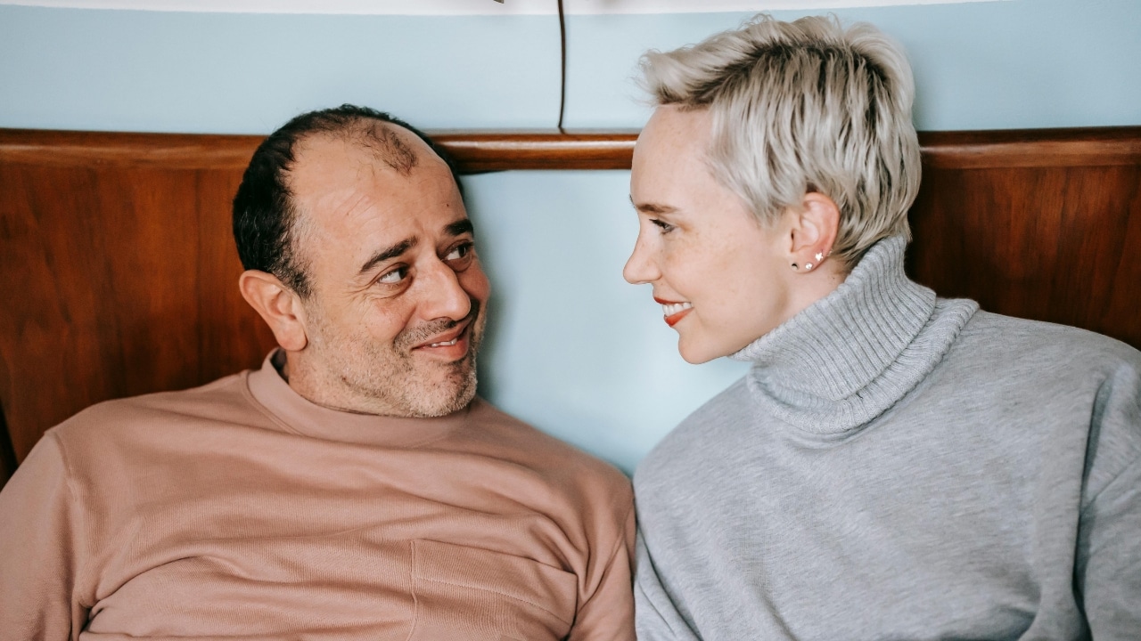 A man and a woman with short blonde hair look at each other smiling.
