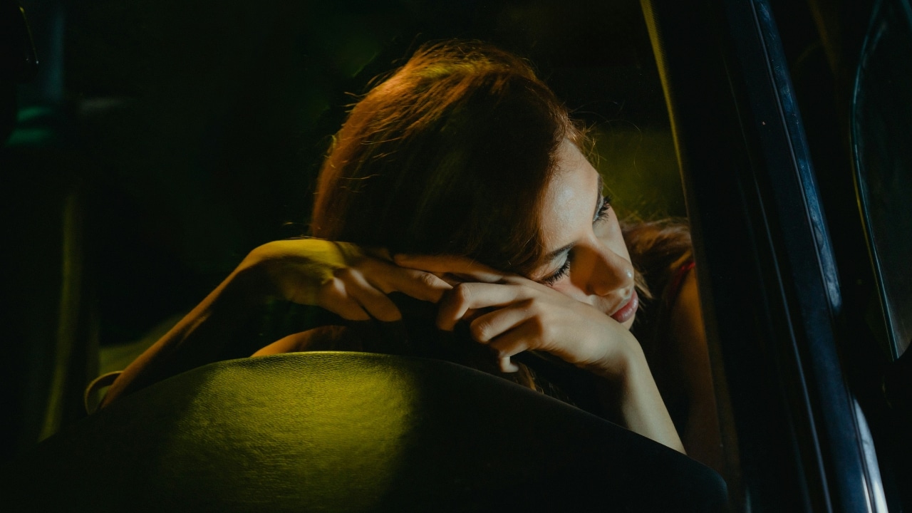 A woman stands in a kitchen holding a glass of water while looking out of a window.