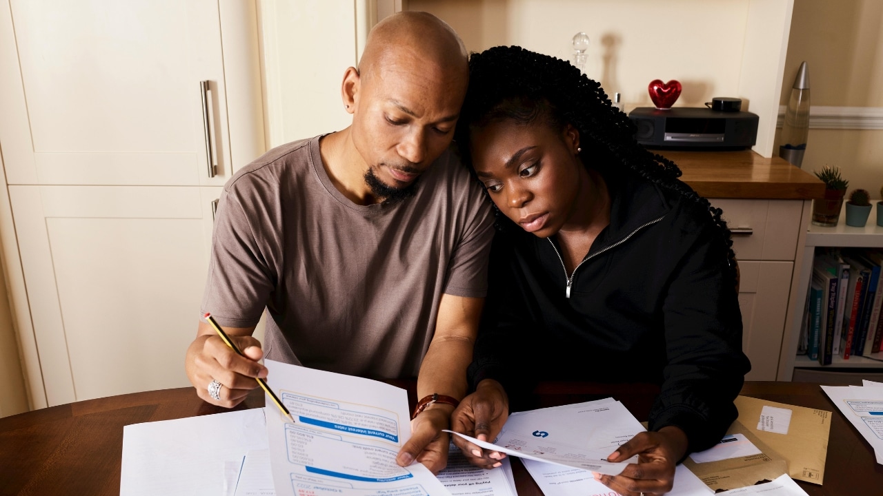 A man and woman sit at a table reviewing several documents and papers together.