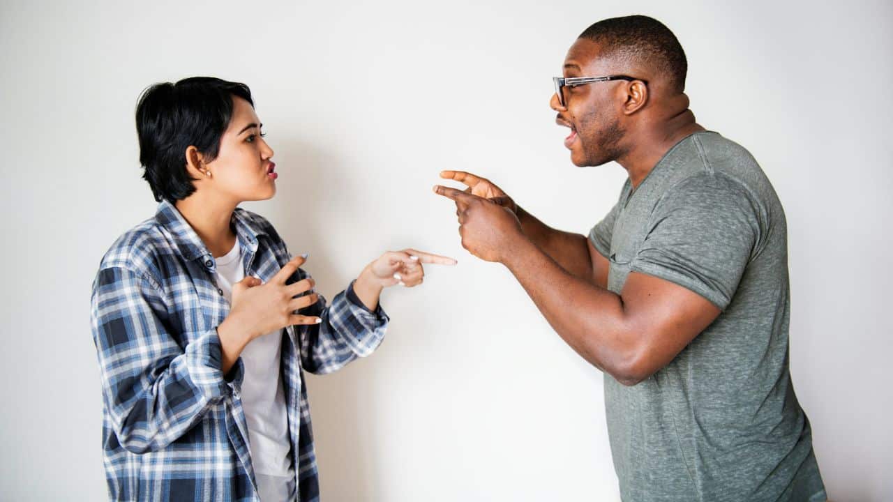 A man and a woman stand facing each other, both gesturing and pointing their fingers.