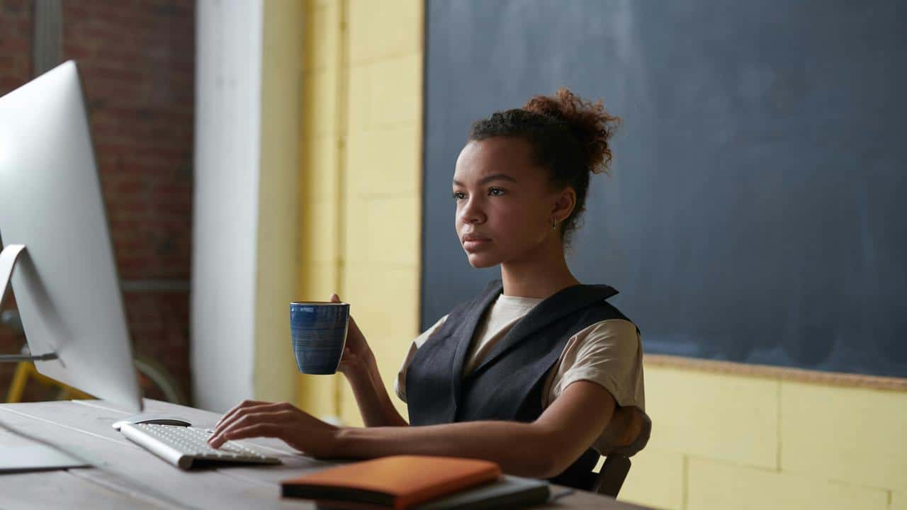 A woman working at a computer while holding a coffee mug.