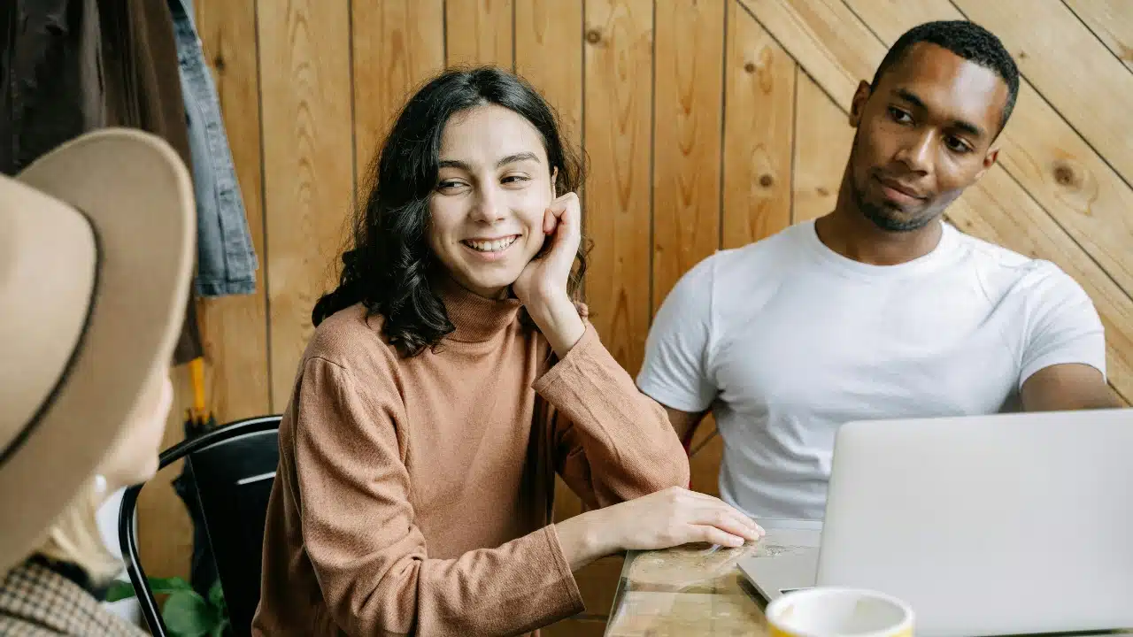 A smiling woman looks toward a man while they both sit at a wooden table.