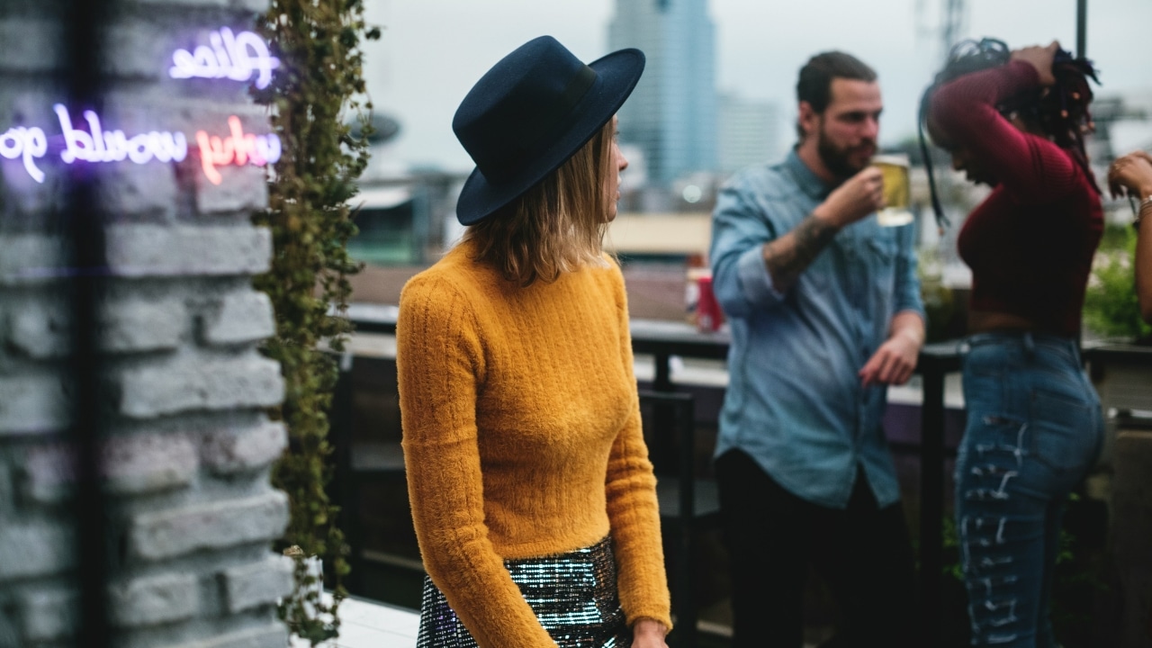 A woman in a yellow sweater and blue hat stands on a rooftop near others.